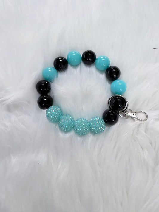 A beaded bracelet with alternating black and turquoise blue beads, featuring five textured turquoise glittery beads on one side and a silver lobster clasp 